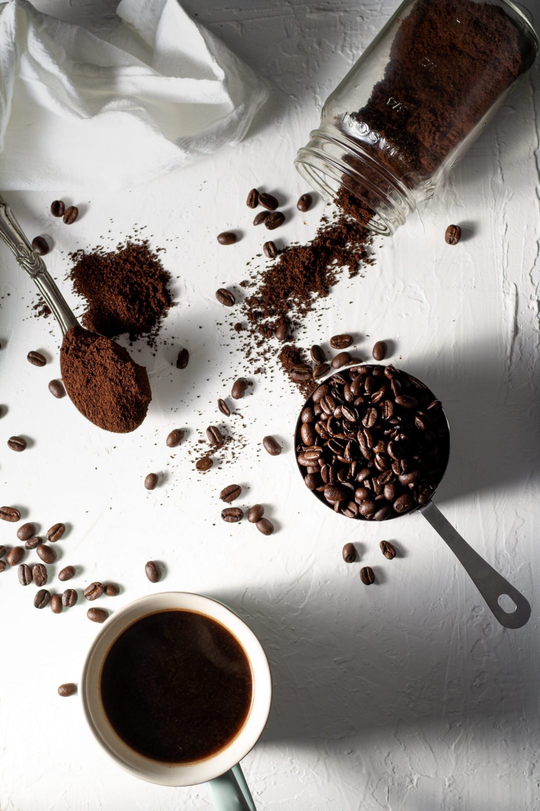 Coffee beans and ground coffee arranged on a white table cloth.